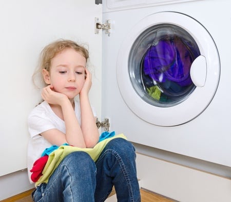 A little girl sitting by the washing machine waiting for clothes to finish spinning