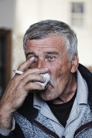 A man drinking and holding a lighted cigarette
